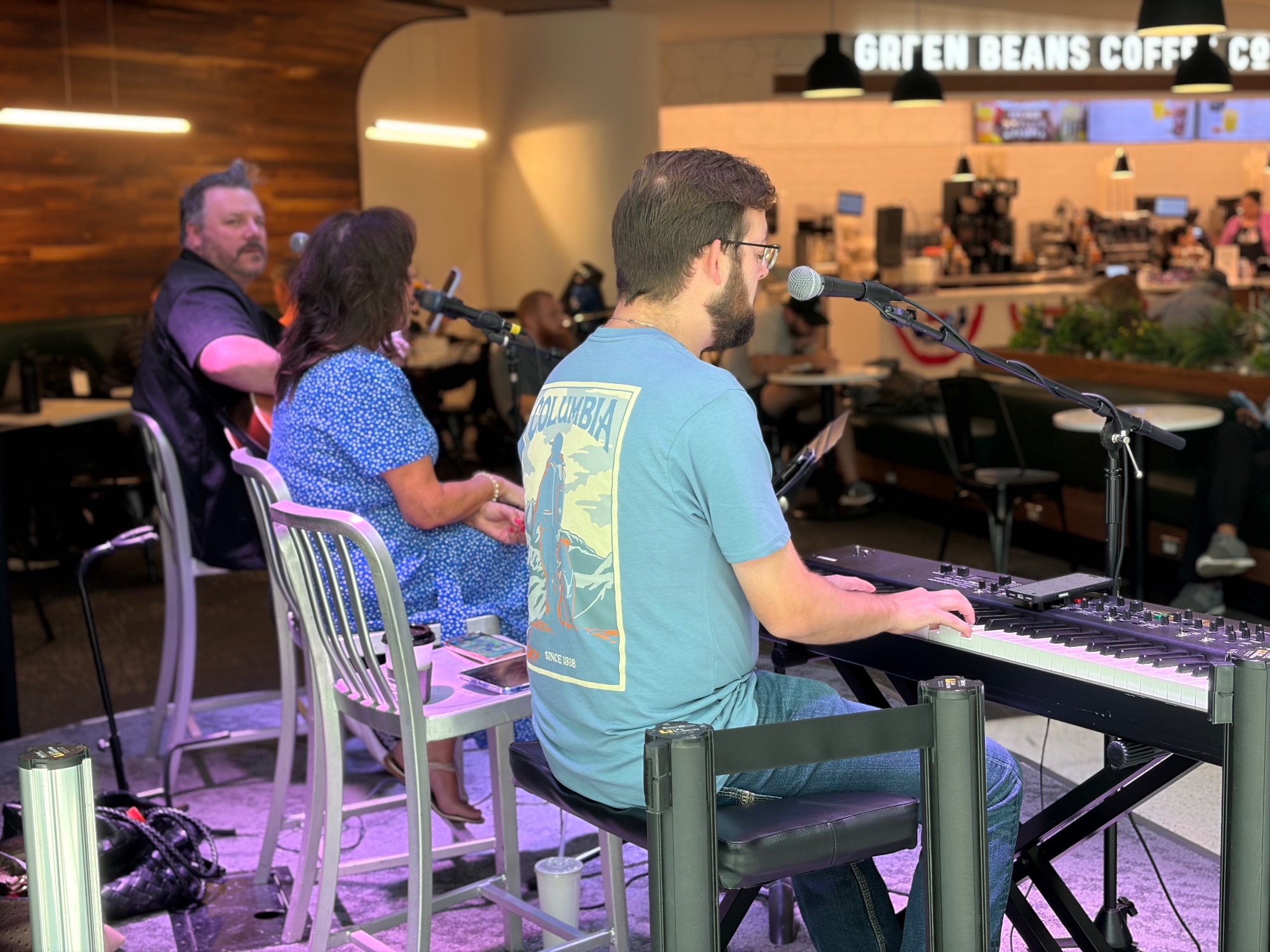 Keyboard player and singers performing at an airport gate as travellers pass behind