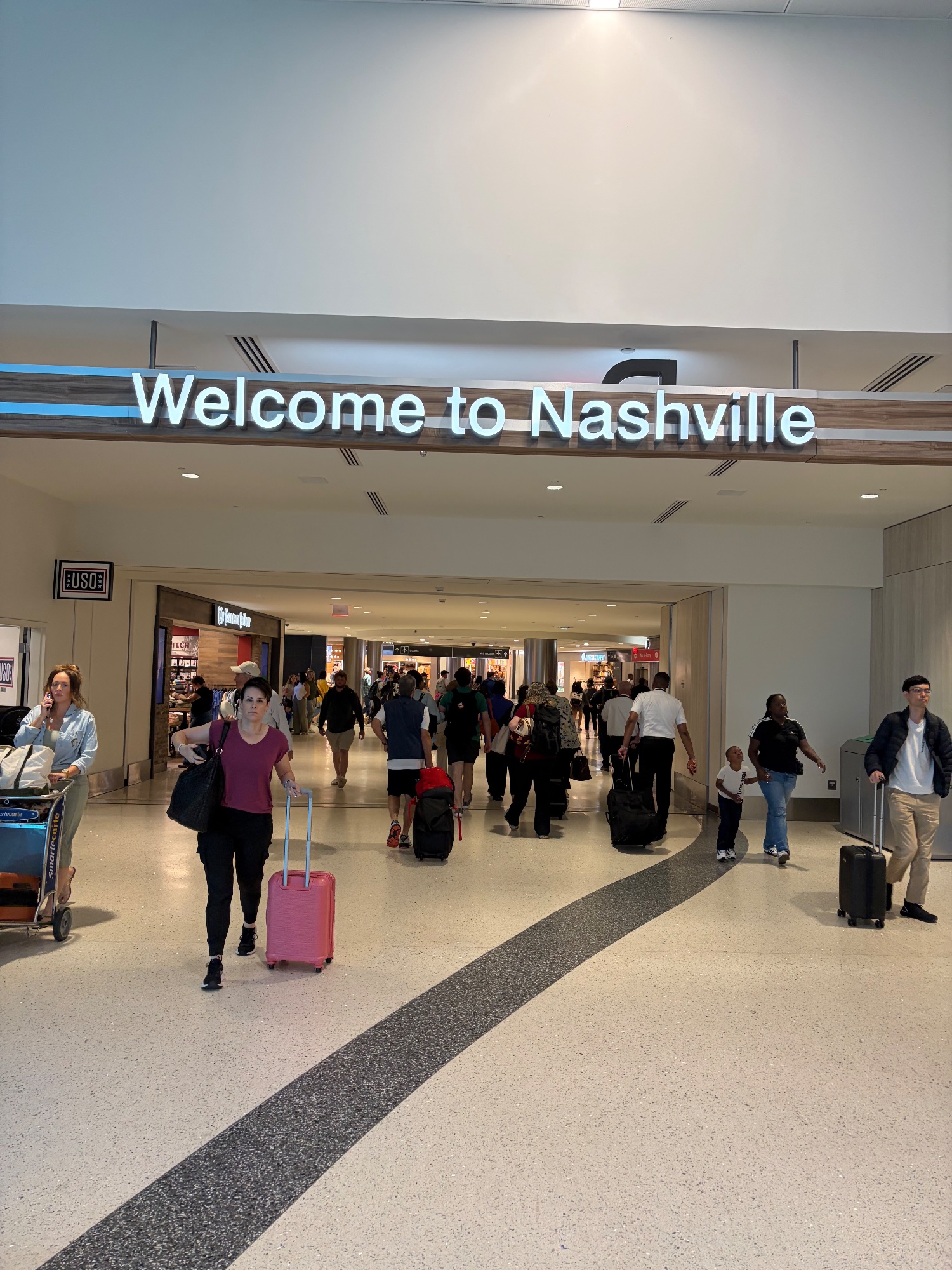 Travellers with luggage beneath a Welcome to Nashville sign in the terminal