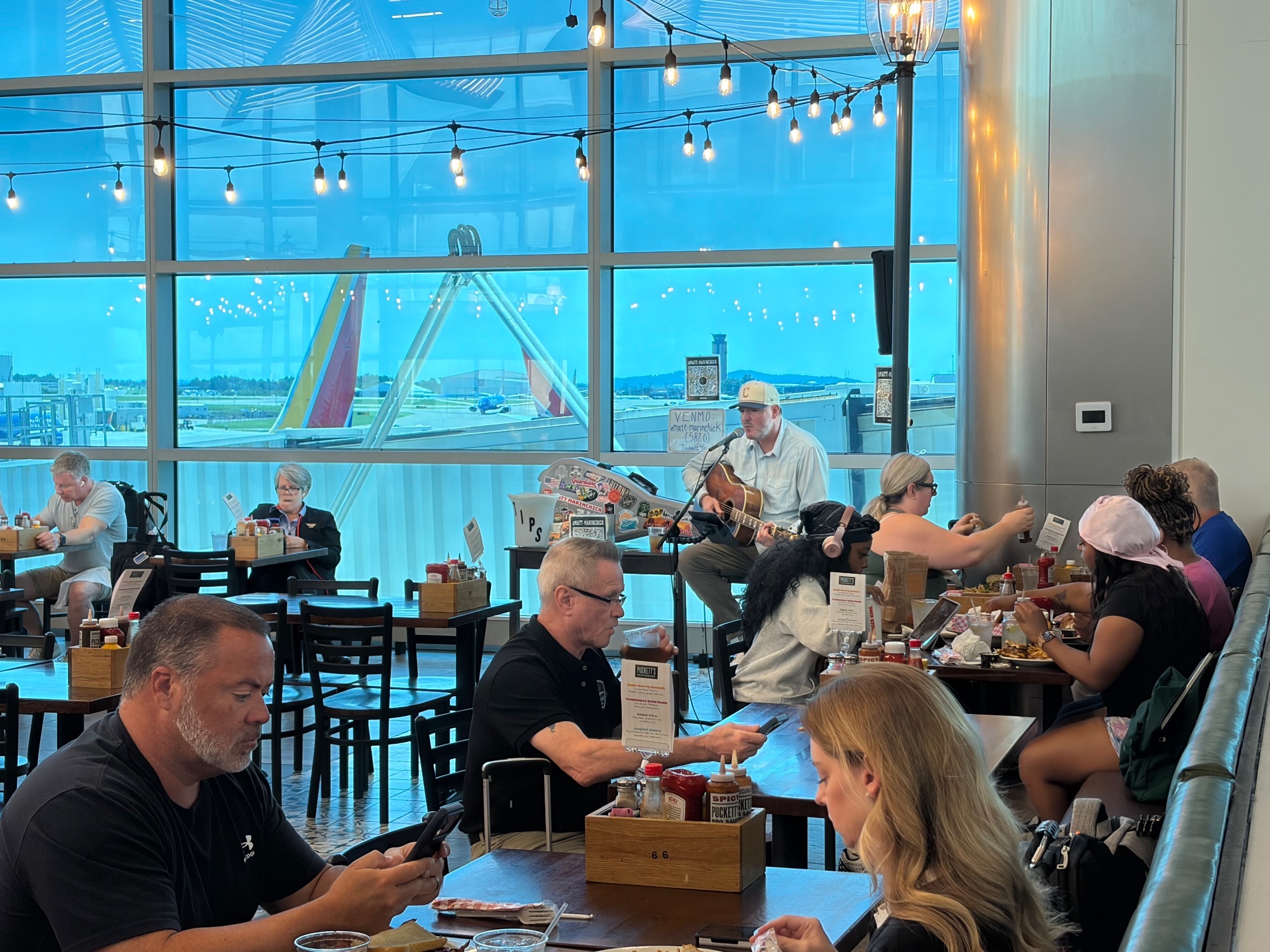 Airport bar under strings of lights, diners at the window with aircraft outside