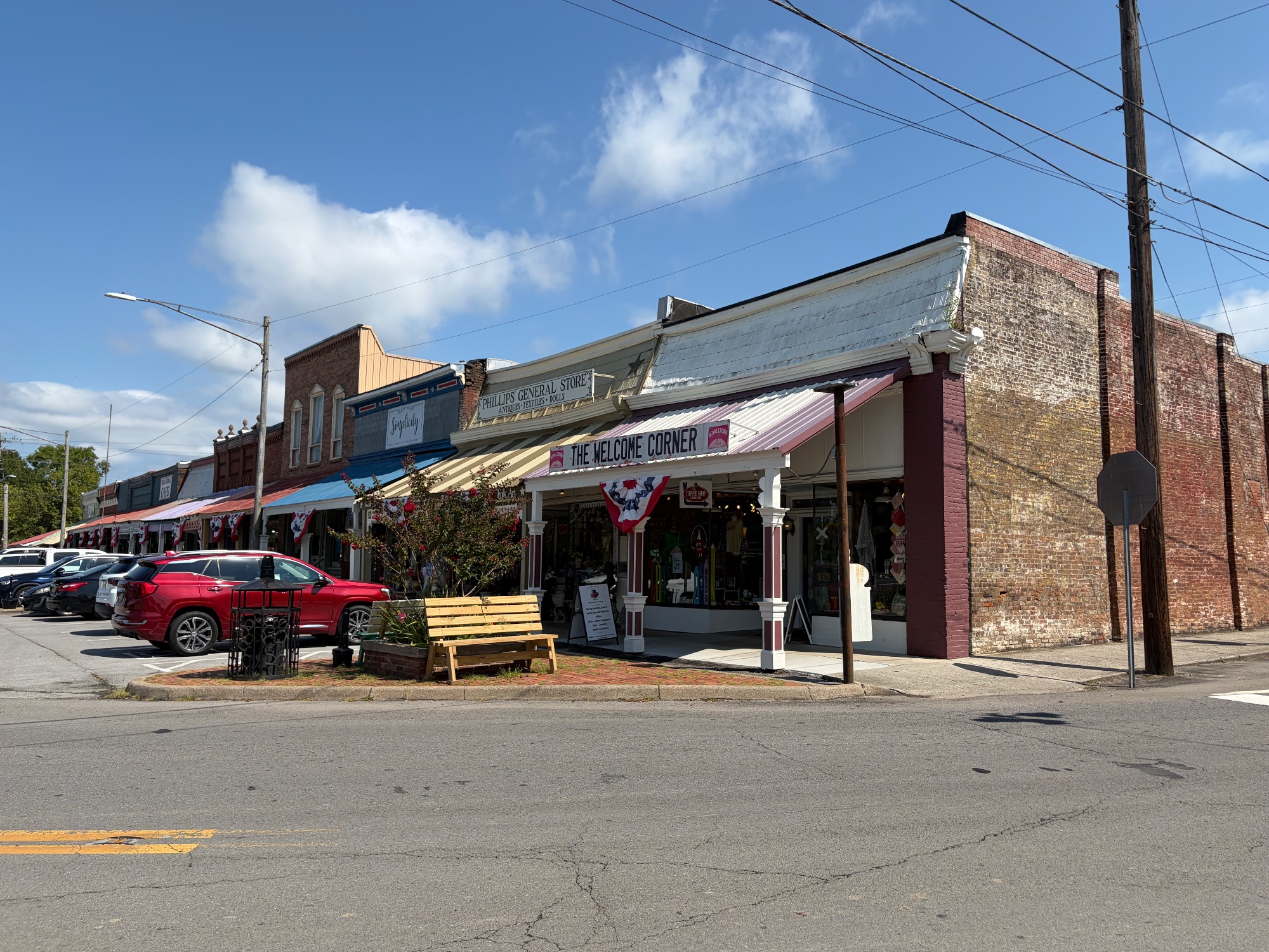 Low shopfronts along a small town main street under a wide blue sky, cars parked at an angle