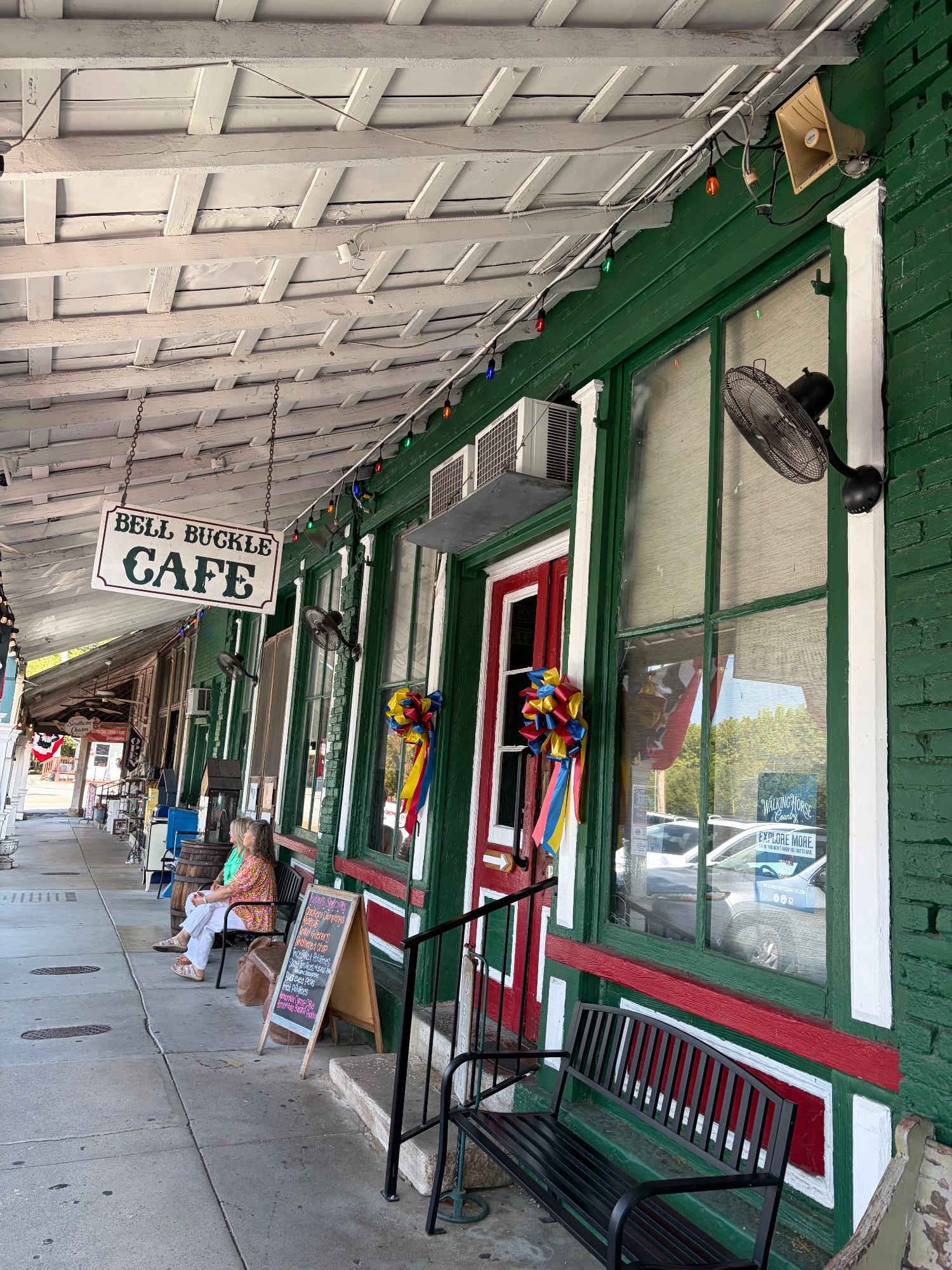 A Bell Buckle Cafe sign hanging from a green painted storefront on a covered sidewalk