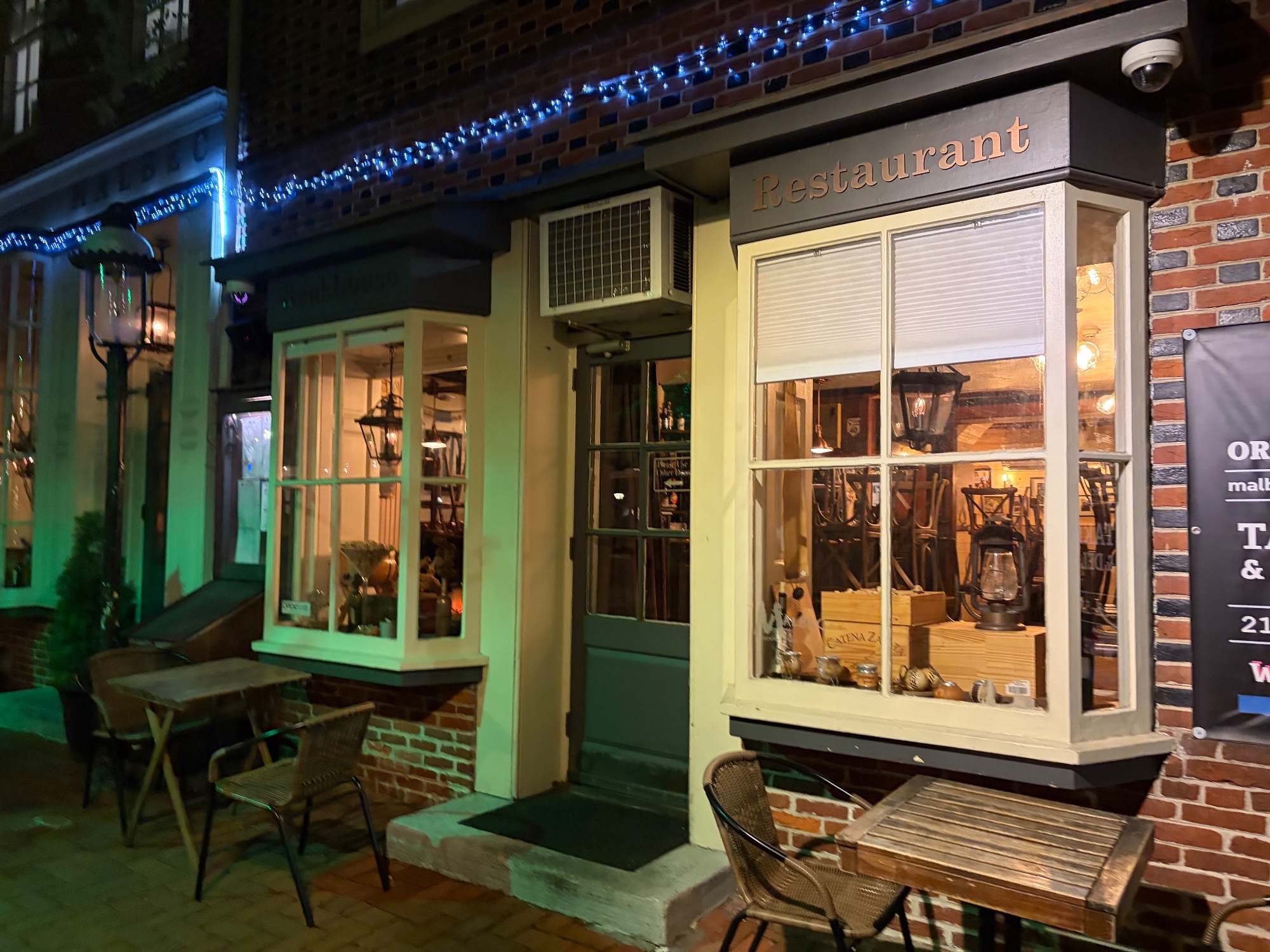 Corner restaurant with bay windows and lanterns glowing inside, brick pavement outside