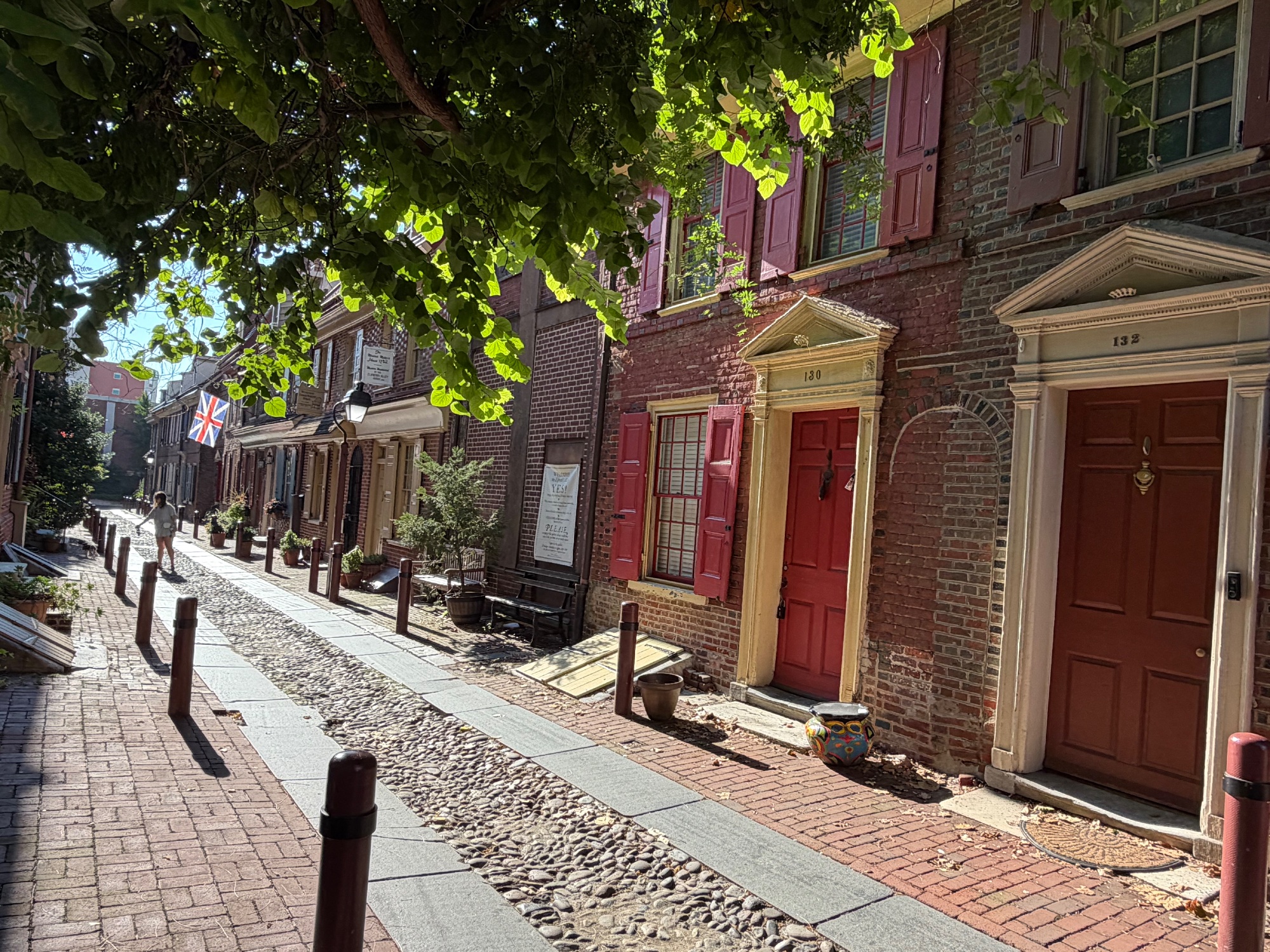 Brick houses with painted doors along a sunlit cobbled alley, flags hanging above